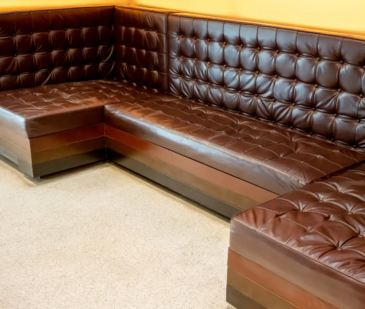 Brown tufted leather corner sofa with no cushions in a room, placed against a yellow wall.