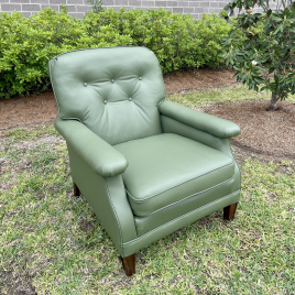 A green chair sitting in the grass near bushes.